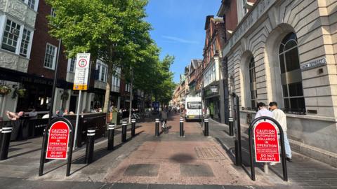 An image of a street with rising bollards preventing entry to cars and warning signs. 