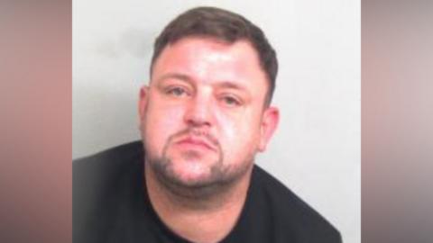 Jakub Konkel pictured in police custody. He has brown hair and is wearing a black jumper.