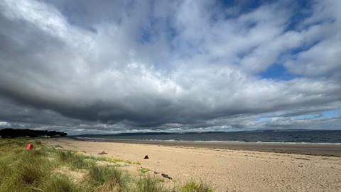 A huge grey, white cloud fills the sky over the sea and a beach
