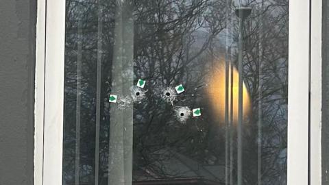 Four small bullet holes are left on a large pane of glass. There are small arrow stickers placed at each hole.