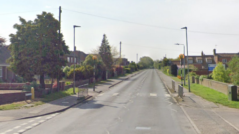 A general view of the Mill Lane junction on Holt Road in Horsford. Holt Road stretches into the distance. A zebra crossing can be seen in the foreground, just before the juntion, which is on the left. Houses line the road on either side. The road has no cars on it.