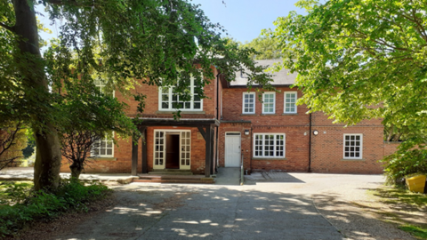 Church View Children's Home. A large red brick country style house with white framed windows. Trees line either side of the driveway on a sunny day. 