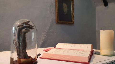 The shrunken hand of 17th century Roman Catholic priest Edmund Arrowsmith sits in a domed glass case on an altar in Arrowsmith House, Brindle, Lancashire. Beside it is a copy of the bible and a candle. 