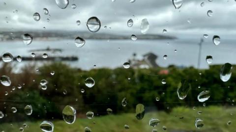 A window looking out onto Douglas Bay - there are raindrops on the window.