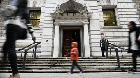 The entrance to the HM Treasury building in London is pictured in a front-on shot with a security guard standing watch while pedestrians walk past, taked in London in October 2021