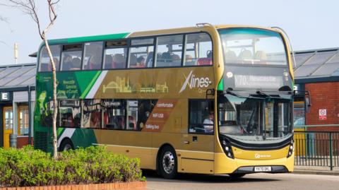 A yellow double decker X70 bus to Newcastle pulling away from a bus station