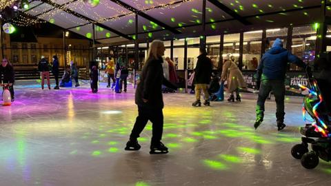 People skating around an ice rink with a green disco light projecting on to the ice