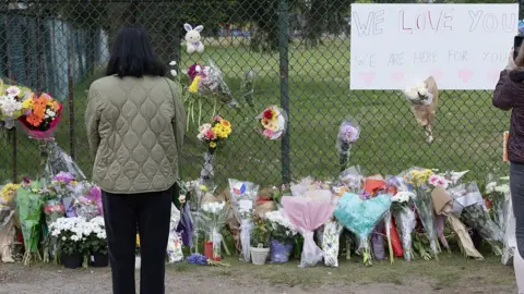 Woman facing away from camera, line of flowers next to fence.