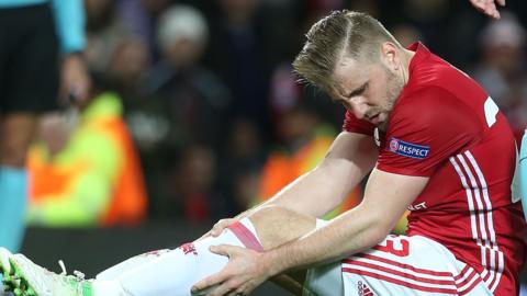 Luke Shaw Man Utd player holds leg while sitting on the pitch