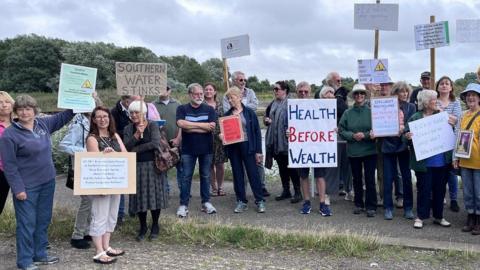 Havant protest group stand in an arch with water behind them holding placards