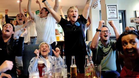 Football fans jumping for joy in a pub. 