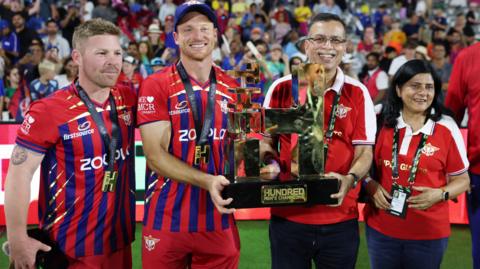 Manchester Super Giants captain Jos Buttler and owner Sanjiv Goenka hold up the 2026 men's Hundred trophy, with opener Tim Seifert (left) and Goenka's wife Preeti (right) flanking them
