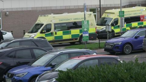 Several vehicles are pictured in a car park, while two ambulances line up in front of a building.