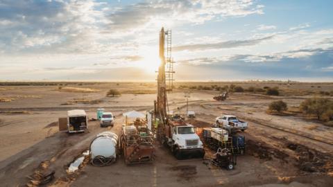 Image of machinery and work trucks on a brown field - the site of Ivanhoe Mining Ltd's Santa Cruz project in Arizona - with the sun setting behind the machinery
