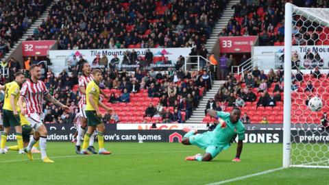 Wrexham and Stoke players watch as the ball passes Wrexham goalkeeper Arthur Okonkwo into the net 