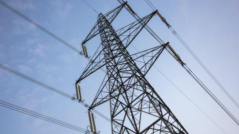 An electricity pylon against a blue sky with tiny clouds.