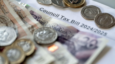 A close up of a £20 note, two £10 notes, pound coins, 50p coins, 20p coins and a 10p coin all lying on top of a white piece of paper that reads Council Tax Bill 2024/2025.
