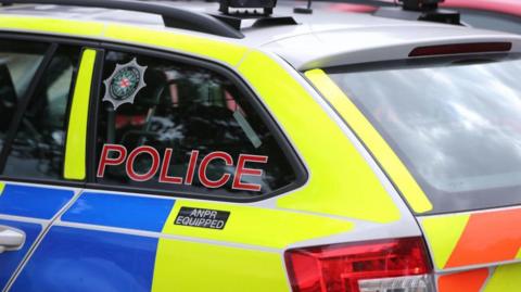 A police car which is yellow and blue in colour. Police is written on the side in red letters.