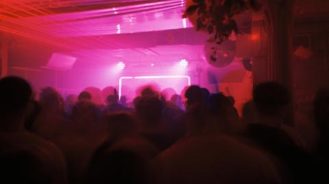 Inside Cobalt during a club night which is filled with people who are slightly blurred and cast in shadow. The lights are pink and there is a light up lit up rectangular structure towards the back of the room.