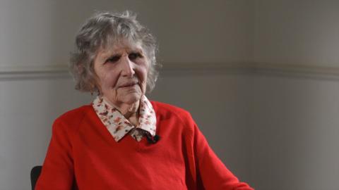 Olga Henderson wearing a red jumper looking off camera being interviewed about her WW2 experience