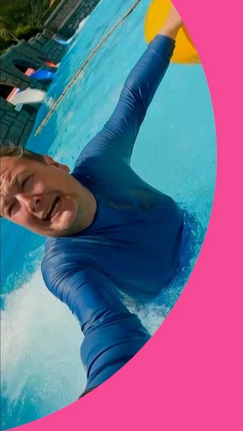 Alan Carr grimacing in a swimming pool holding a selfie stick.