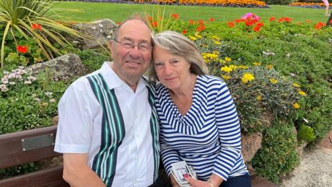 Anthony and Pat Davies sitting on a bench with grass and flowers in the background