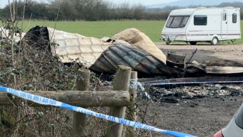 A burnt motorhome in a field with other caravans. The only part of the mobile home identifiable is a plastic roof. 