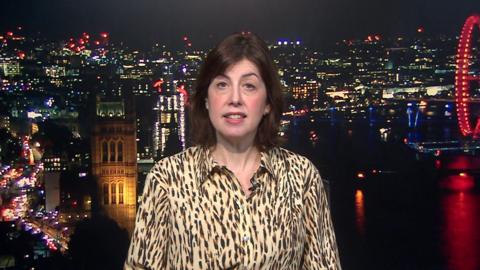 Lucy Powell has shoulder-length brown hair. She wears a patterned shirt and sits in a BBC studio with a background of the London skyline.