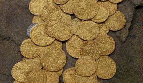 Pile of scattered gold coins and one silver coin seen on the edge of the picture in the top left.