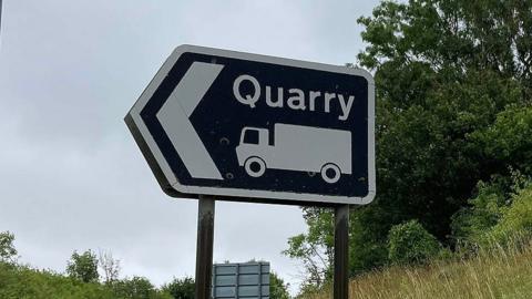 Generic street sign saying quarry with a picture of a lorry underneath and an arrow pointing to the left