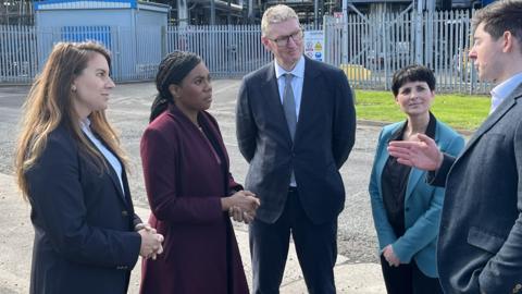 Two men and two women stand around Conservative Party leader Kemi Badenoch and speak to her outside on the grounds of Huntsman. All five people are wearing formalwear and Badenoch is looking and one of the men and listening to him.