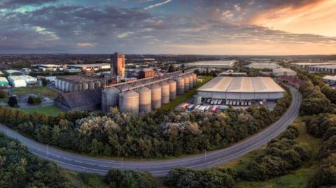 A drone shot of a road circling around an industrial site surrounded by trees during the sunrise.