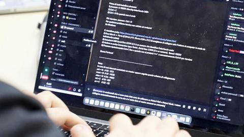 A computer keyboard with code on it and the operator's hands.