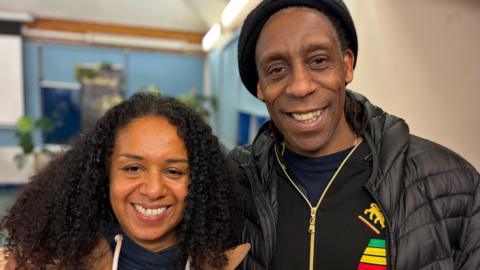 A picture of married couple Amanda Sterling-Bynoe and Derek Sterling smiling towards camera, at the family history masterclass. She has long black curly hair and he has a black hat on