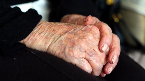 Stock image of clasped hands. The fingernails have chipped nail polish and there are wrinkles on the hands.