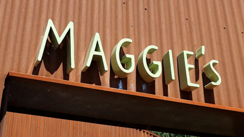 The sign of a Maggie's Centre. The word is in a light green colour on an orange corrugated metal background.
