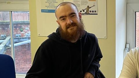 Max Holwell, a smiling young man with a shaved head and a long beard.