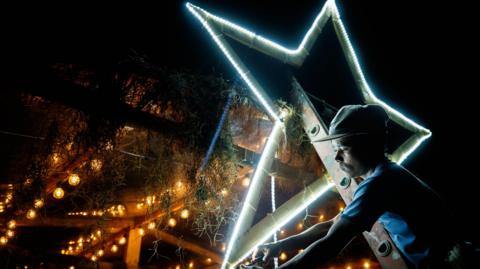 Man decorating a Christmas stall with a large  light up star decoration 