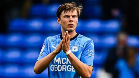 Oscar Wallin applauds fans after an appearance for Peterborough United