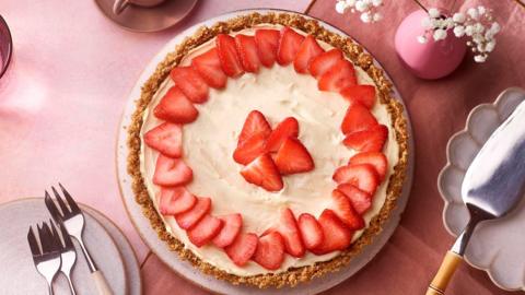 A round, creamy tart on a biscuit base, topped with sliced strawberries.