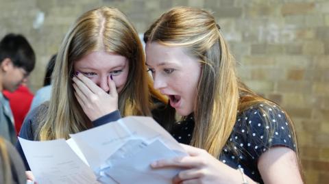Two students collect their GCSE results and have an open-mouthed expression