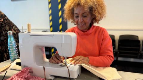 A women wearing an orange jumper using a white sewing machine