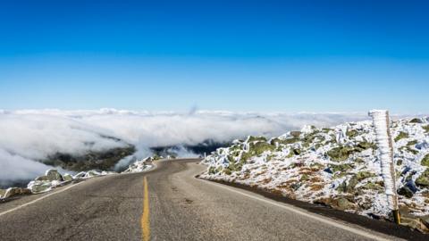 a winding road into a layer of clouds with blue sky above