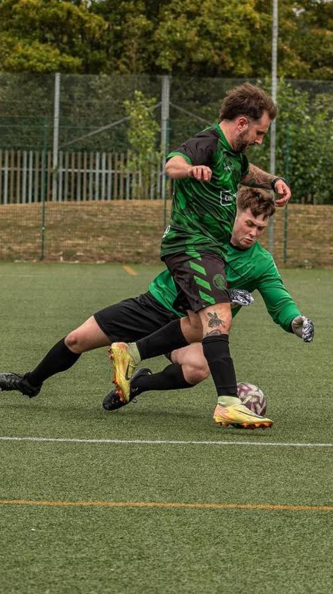 Two men playing football, one attacker attempting in go past a diving goalkeeper
