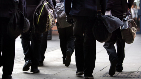 A group in school uniform, carrying bags, are walking away from the camera. None of them can be identified.