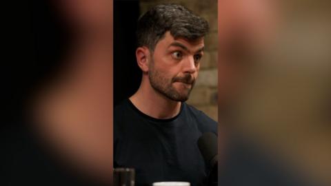 A man with short, dark hair looks across at someone