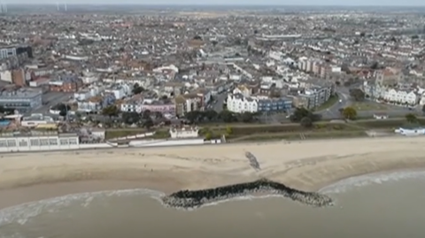 A drone view of a beach from above. You can see the beach and the city in the shot as well
