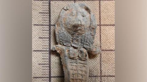 A close up picture of the medieval doll. Hair and eyes are easy to make out as well as short arms and breasts.