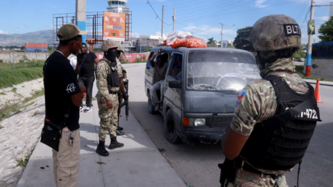 Police officers in protective fatigues and bullet-proof vests stand around a beat-up van at a checkpoint near Port-au-Prince's airport during ongoing armed clashes in the city this week