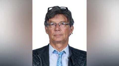 Barry Martin wears a blue tie and shirt and two pairs of glasses, one perched on top of his head. 